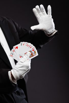 Hands of magician holding cards. Wearing black suit. Studio shot against black.